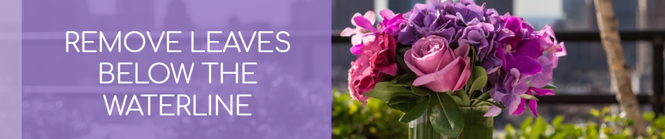 An image of pink and purple flowers in a clear vase on a table outside